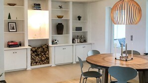 A modern dining area with a round wooden table, two chairs, a chandelier, and built-in shelving with various items. - 4 Star Holiday Home in Storvorde (Storvorde)