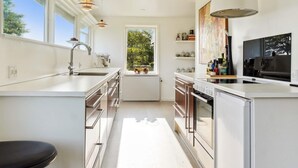 A modern kitchen with white cabinetry, a central island, a large window, and a pendant light. - 4 Star Holiday Home in Storvorde (Storvorde)