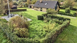 A modern house with a sloped roof, surrounded by well-maintained lawns and hedges. - 4 Star Holiday Home in Storvorde (Storvorde)