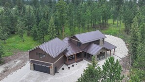 A modern two-story house with a large garage, surrounded by a forested area.