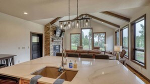 A spacious kitchen with a large island, stone fireplace, and large windows offering views of the outdoors.