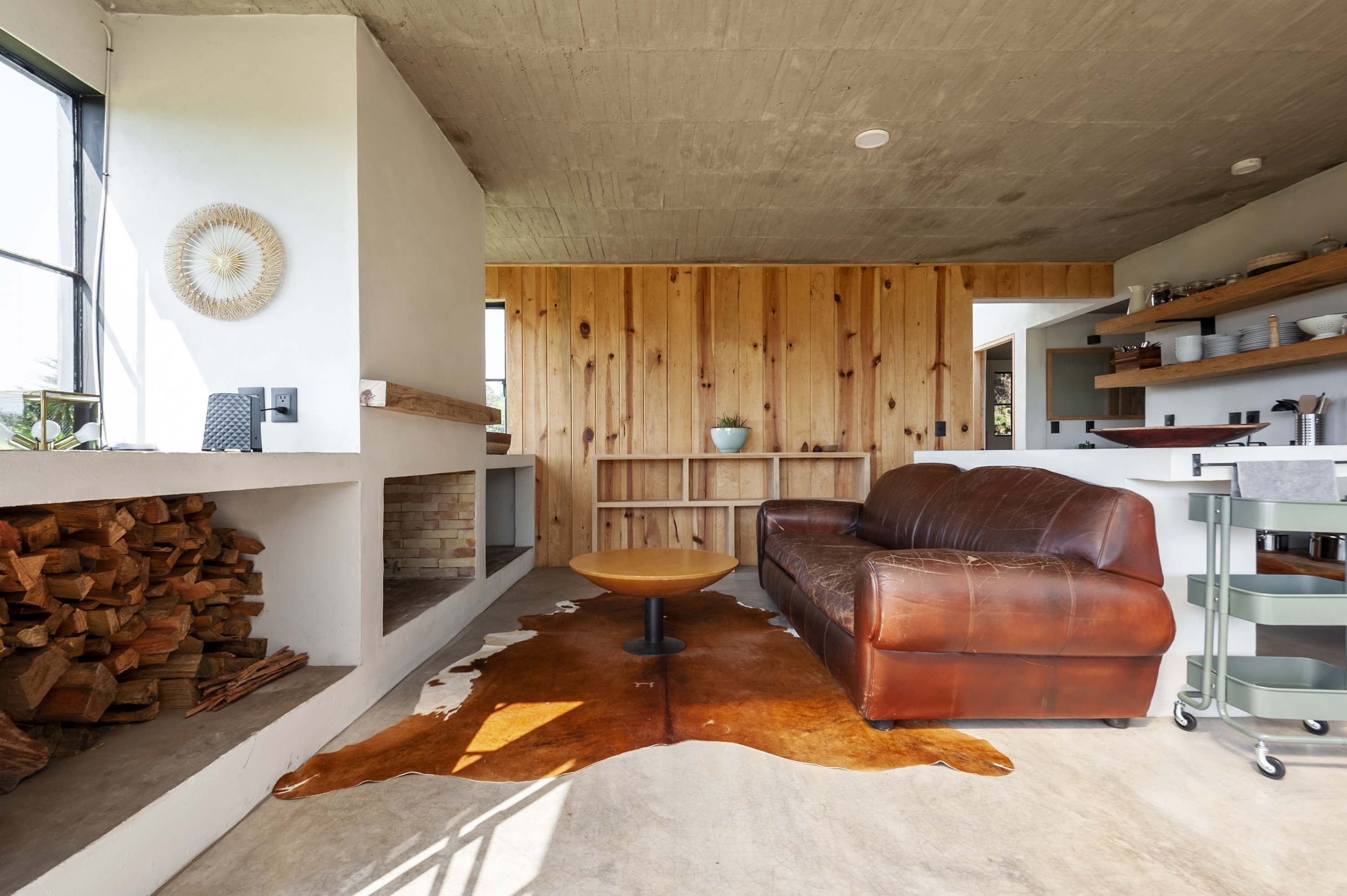 A modern living room with a leather sofa, a round wooden coffee table, and a cowhide rug.