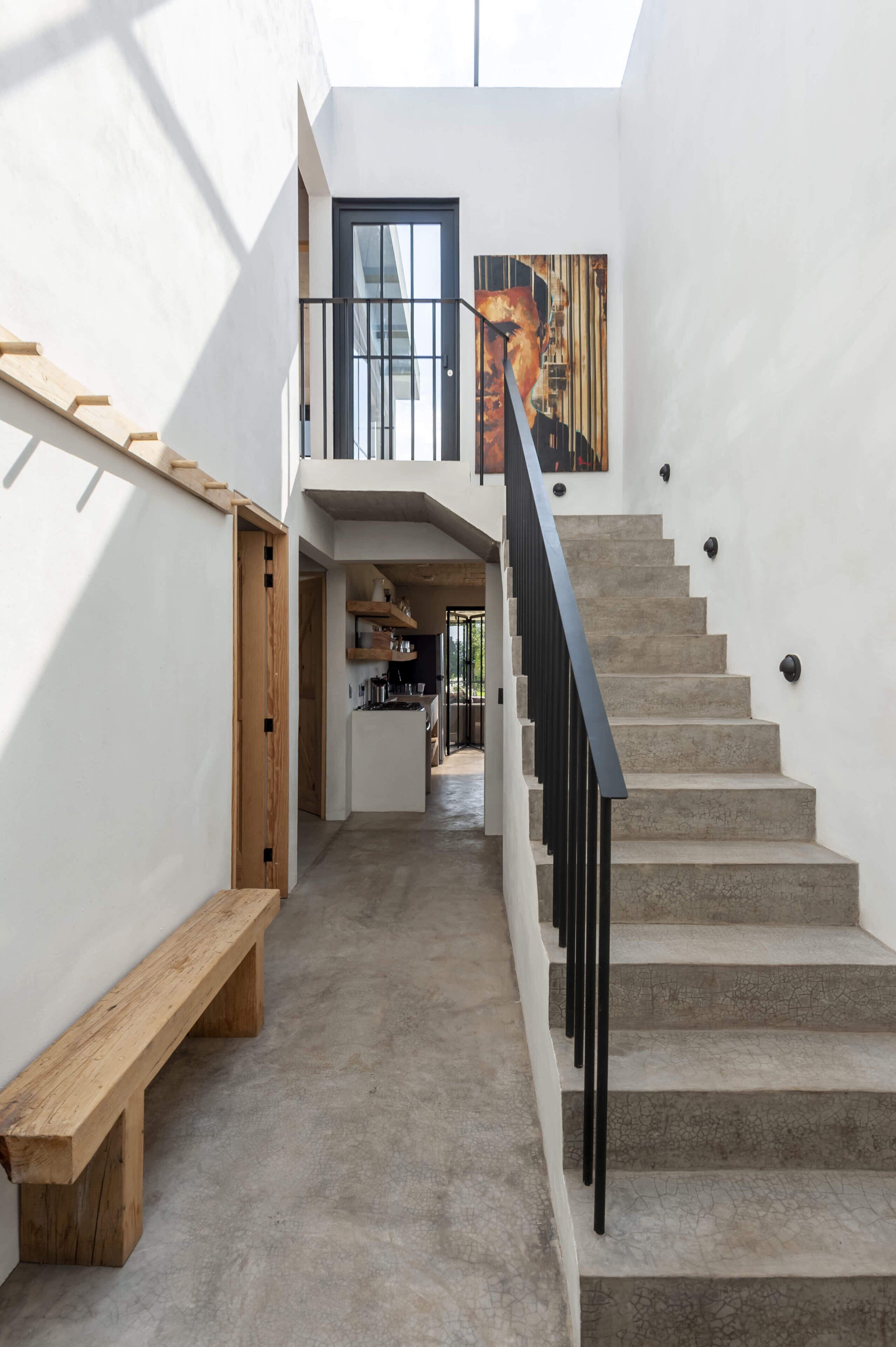 A modern interior with a staircase, wooden bench, and a view of the kitchen area.