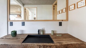 Un baño con tocador de madera, lavamanos negro y un espejo grande.