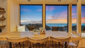 Una mesa de comedor de madera con sillas, ventanas amplias y vista al océano.