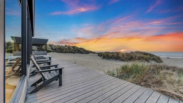 A beach view with a wooden deck, lounge chairs, and a glass wall overlooking the ocean.