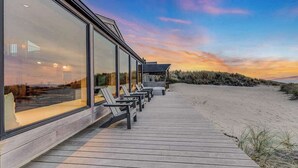 A beachside hotel with a wooden deck, large windows, and beach chairs.