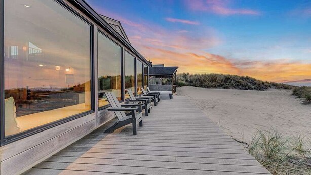 Un hotel frente a la playa con terraza de madera, ventanas amplias y sillas para tomar el sol.