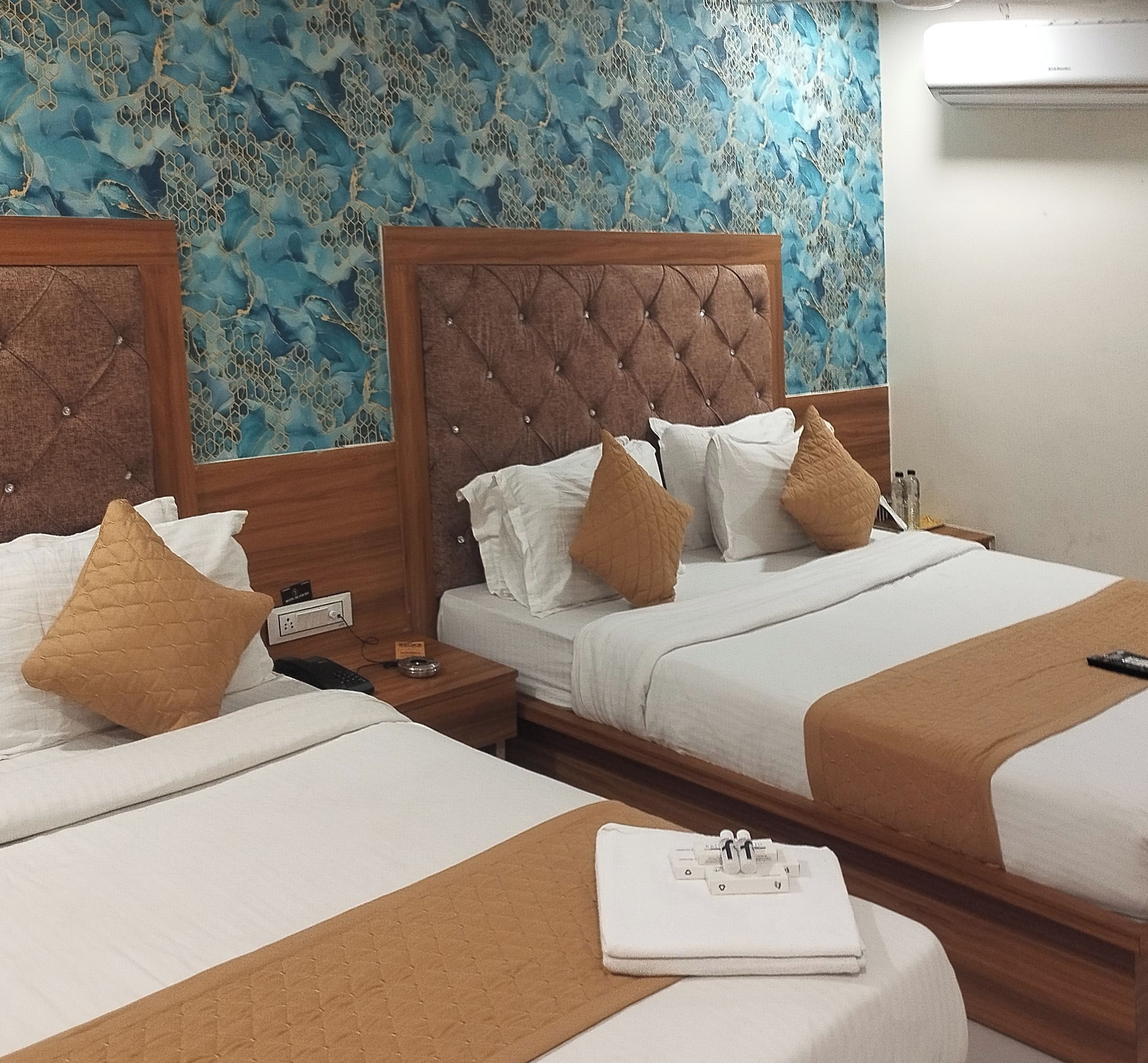 Una habitación de hotel con dos camas, cada una con cabecera de madera, ropa de cama blanca y almohadas marrones. Hay una mesita de noche con un teléfono y un control remoto.