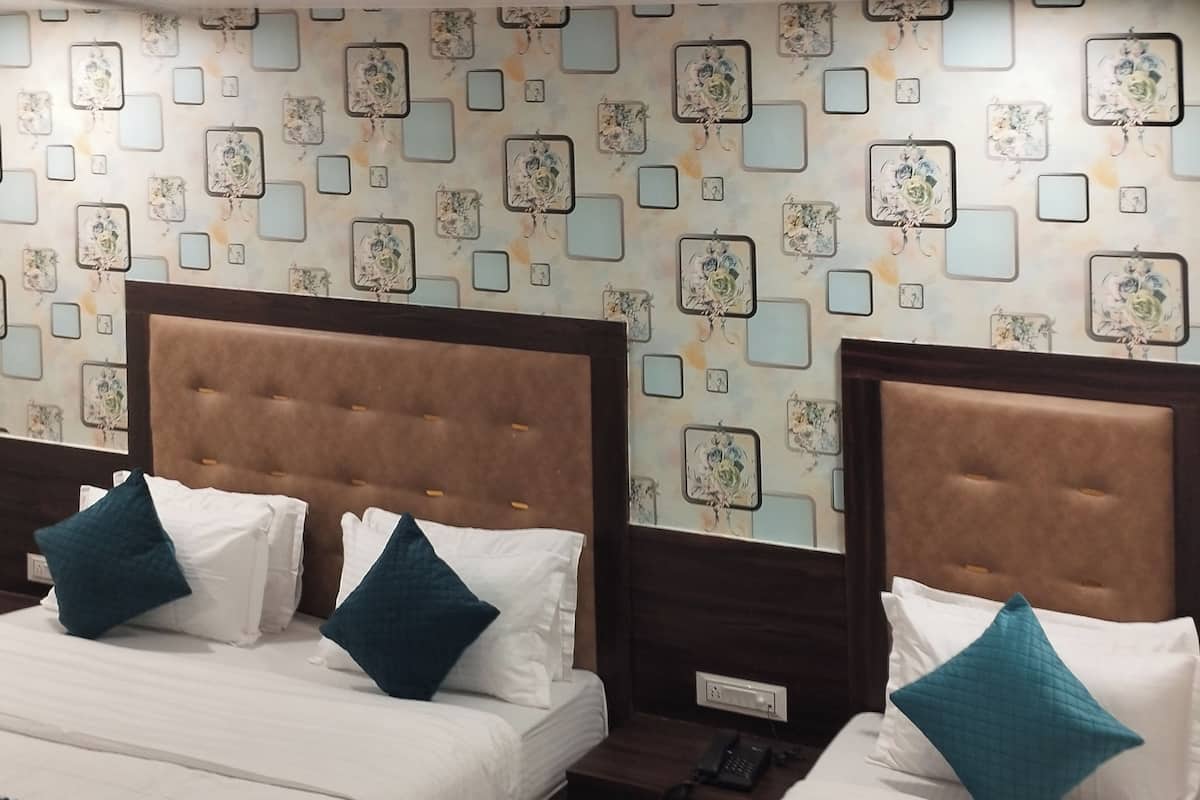 Hotellihuoneessa on kaksi sänkyä, joissa on ruskeat päätyosat, valkoiset vuodevaatteet ja turkoosit tyynyt. Seinissä on kukallinen kuvio, ja siinä on neliönmuotoisia kehyksiä.