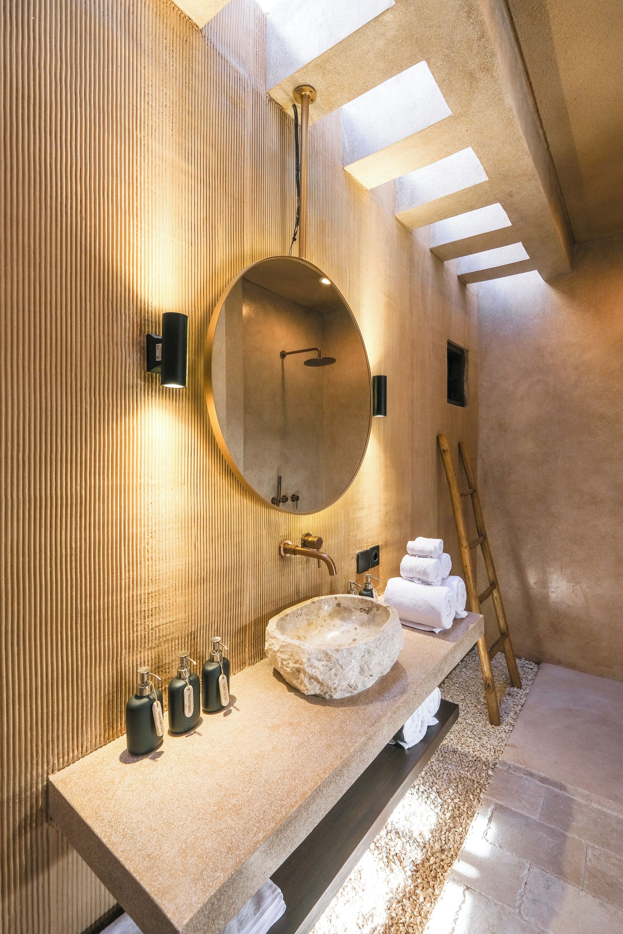 Une salle de bain moderne avec un grand miroir rond, un lavabo en pierre et une échelle en bois.