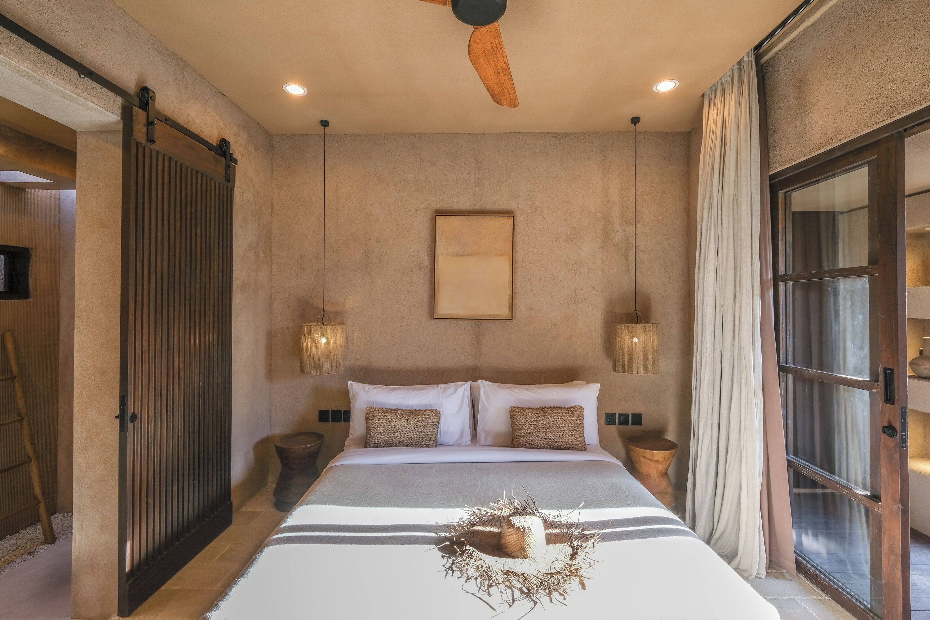 A bedroom with a bed, a ceiling fan, a wall-mounted light, and a window with curtains.