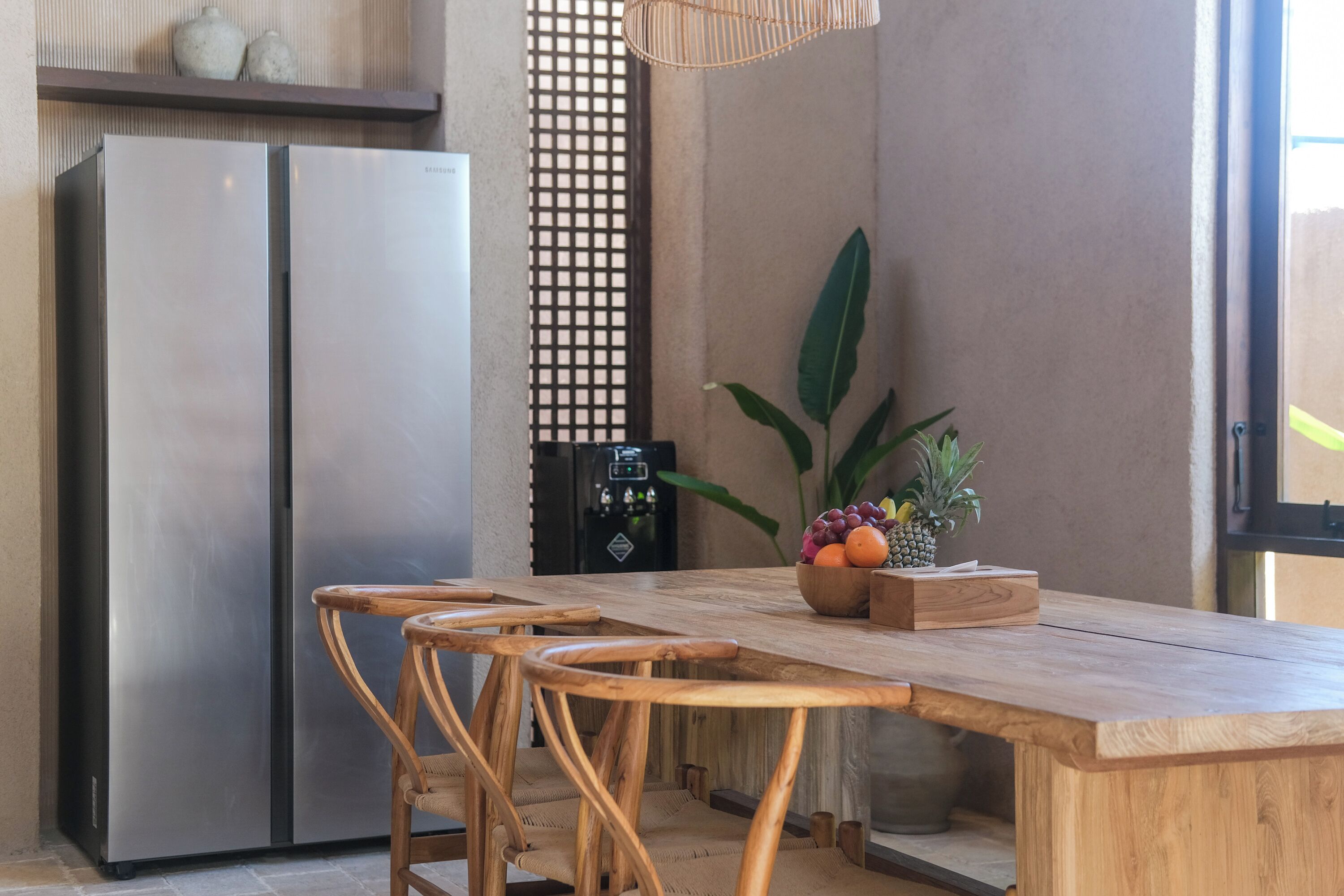 A kitchen with a wooden table, two chairs, a fruit bowl, and a refrigerator.