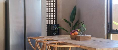 A kitchen with a wooden table, two chairs, a fruit bowl, and a refrigerator.
