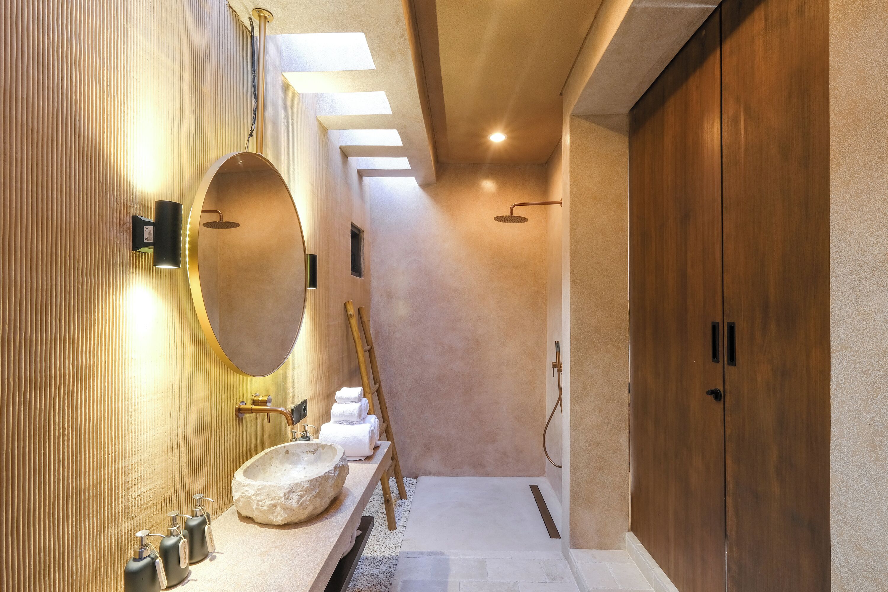 A modern bathroom with a large round mirror, a stone sink, and a wooden vanity.