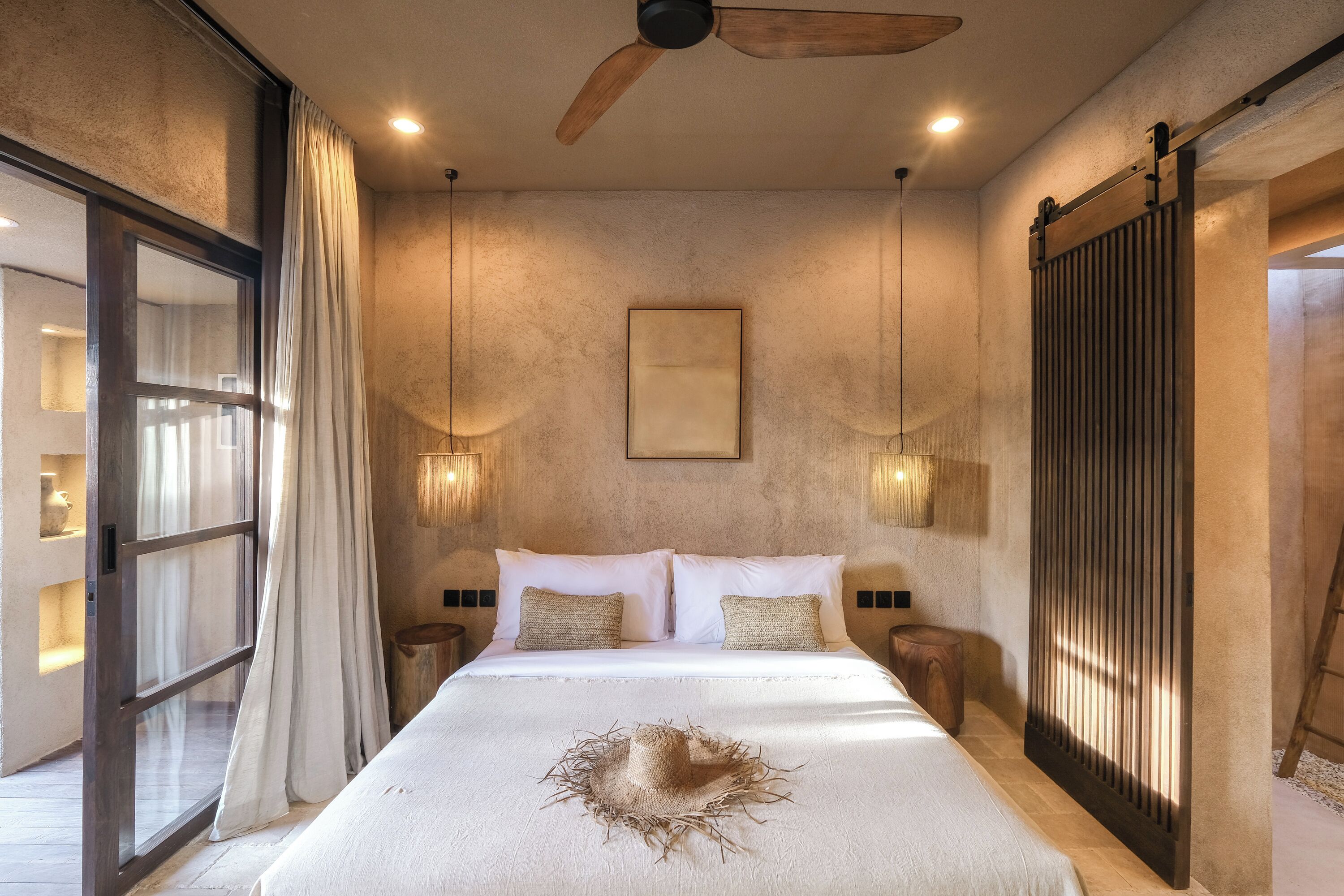 Un dormitorio con una cama grande, ventilador de techo y puerta corredera.