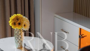 Et rum med et rundt marmorbord, en barstol med gylden ramme, en vase med gule blomster og et hvidt skab med en gylden håndtag.