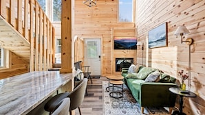 A wooden cabin interior with a dining area, a green sofa, and a fireplace. - Christmas in Modern Mt Cabin-Dollywood, Downtown, Zipline w/ Hot Tub,Grill,Games (Sevierville)