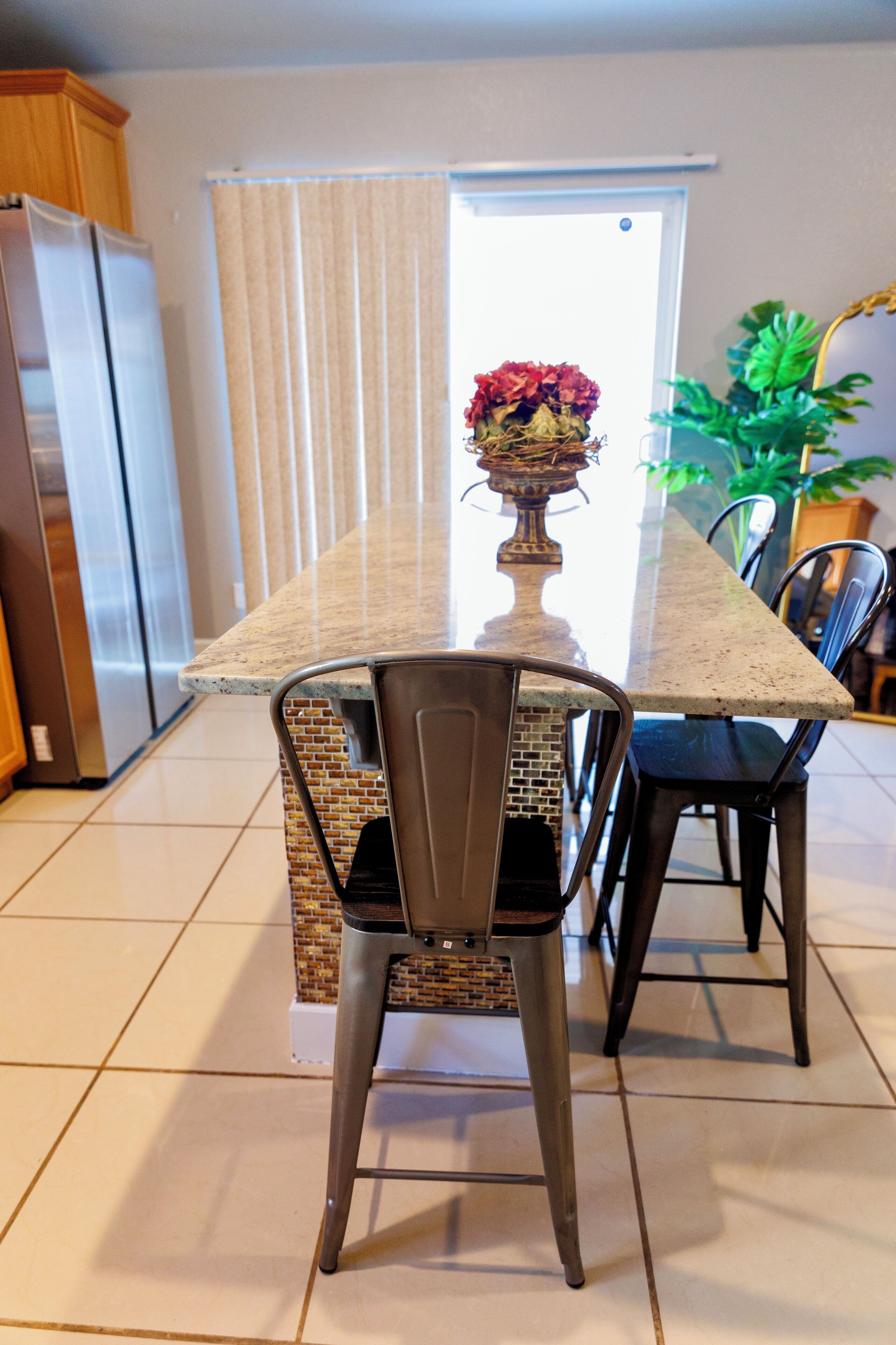 A kitchen with a marble countertop, a dining table, chairs, a refrigerator, and a potted plant.