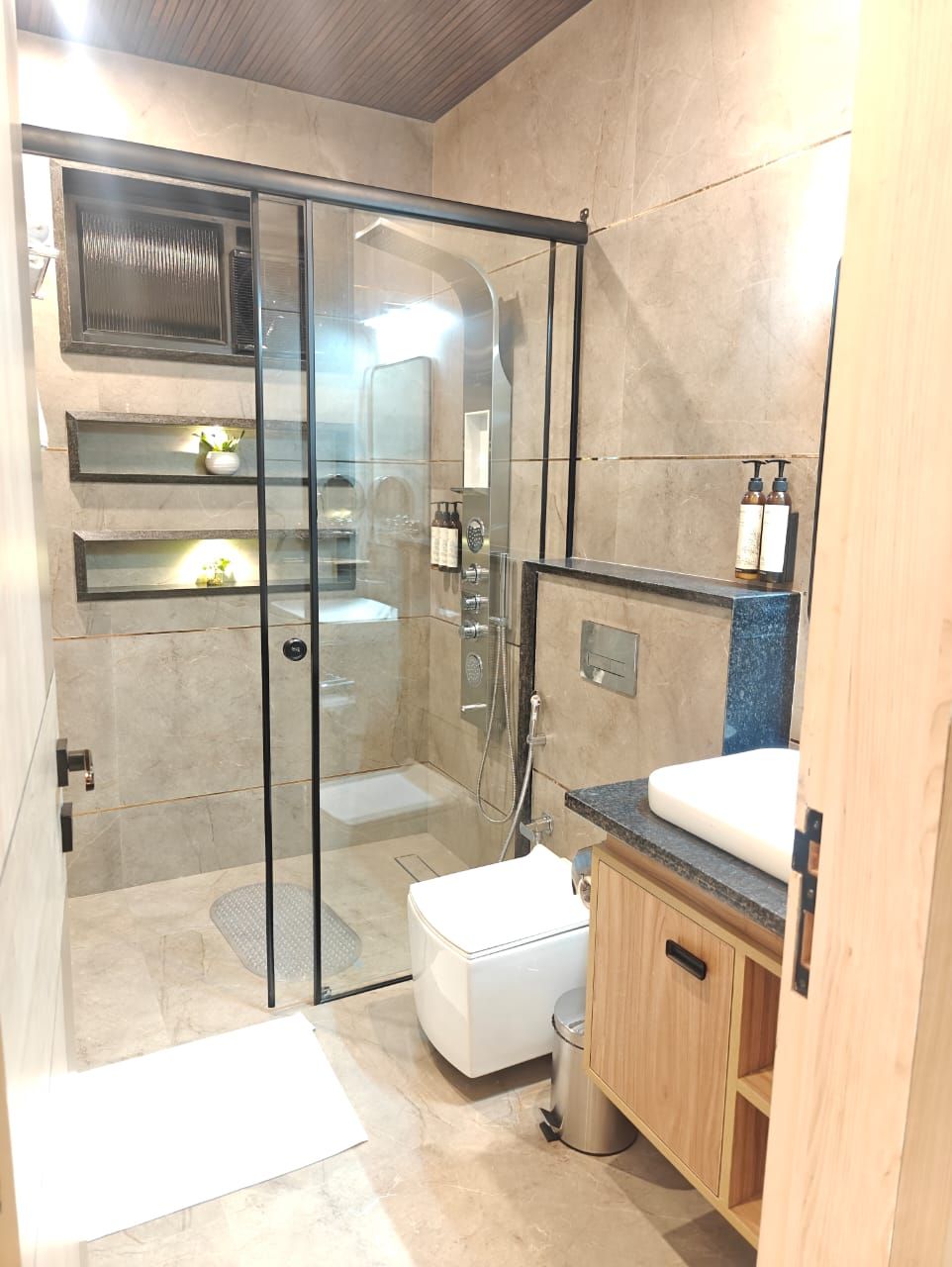 A modern bathroom with a glass-enclosed shower, a white toilet, a wooden vanity with a sink, and a mirror.