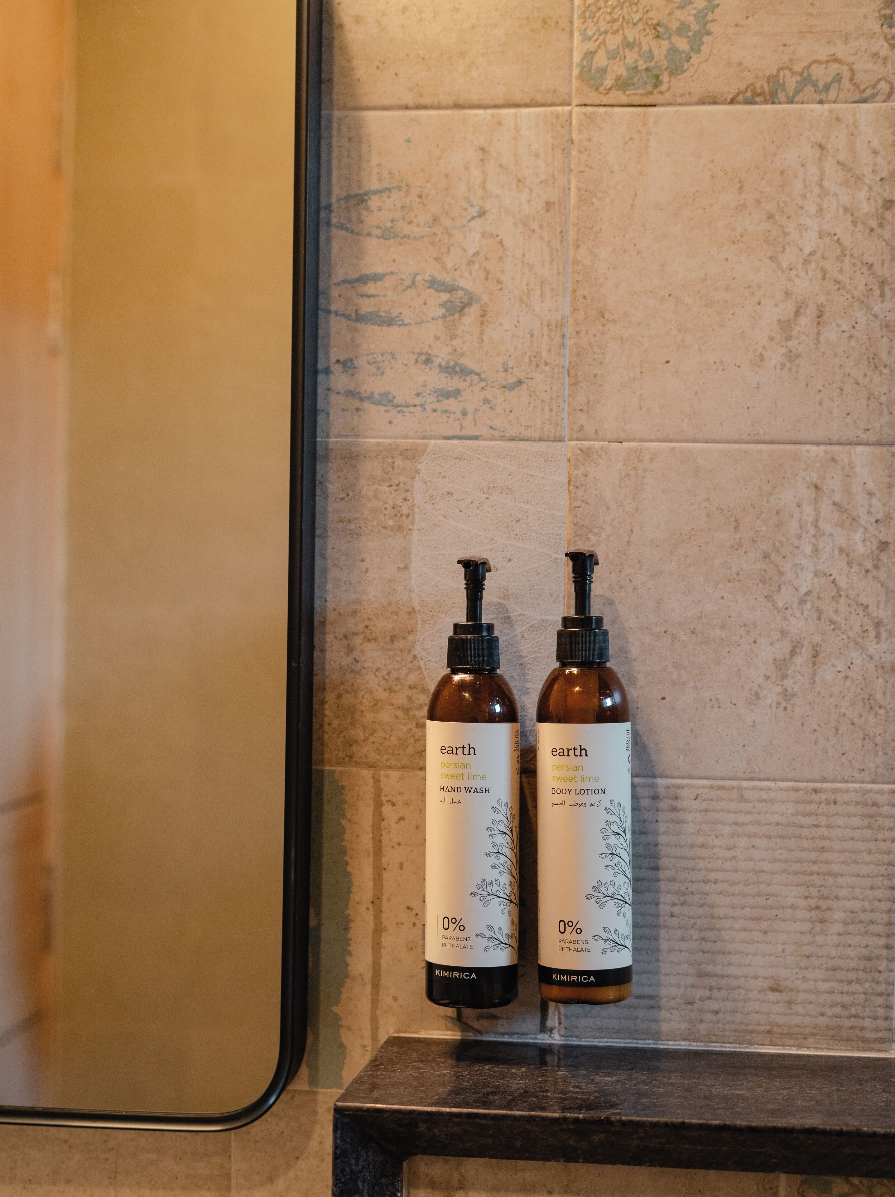Two bottles of 'earth' Persian sweet lime hand wash and body lotion on a dark countertop against a tiled wall.