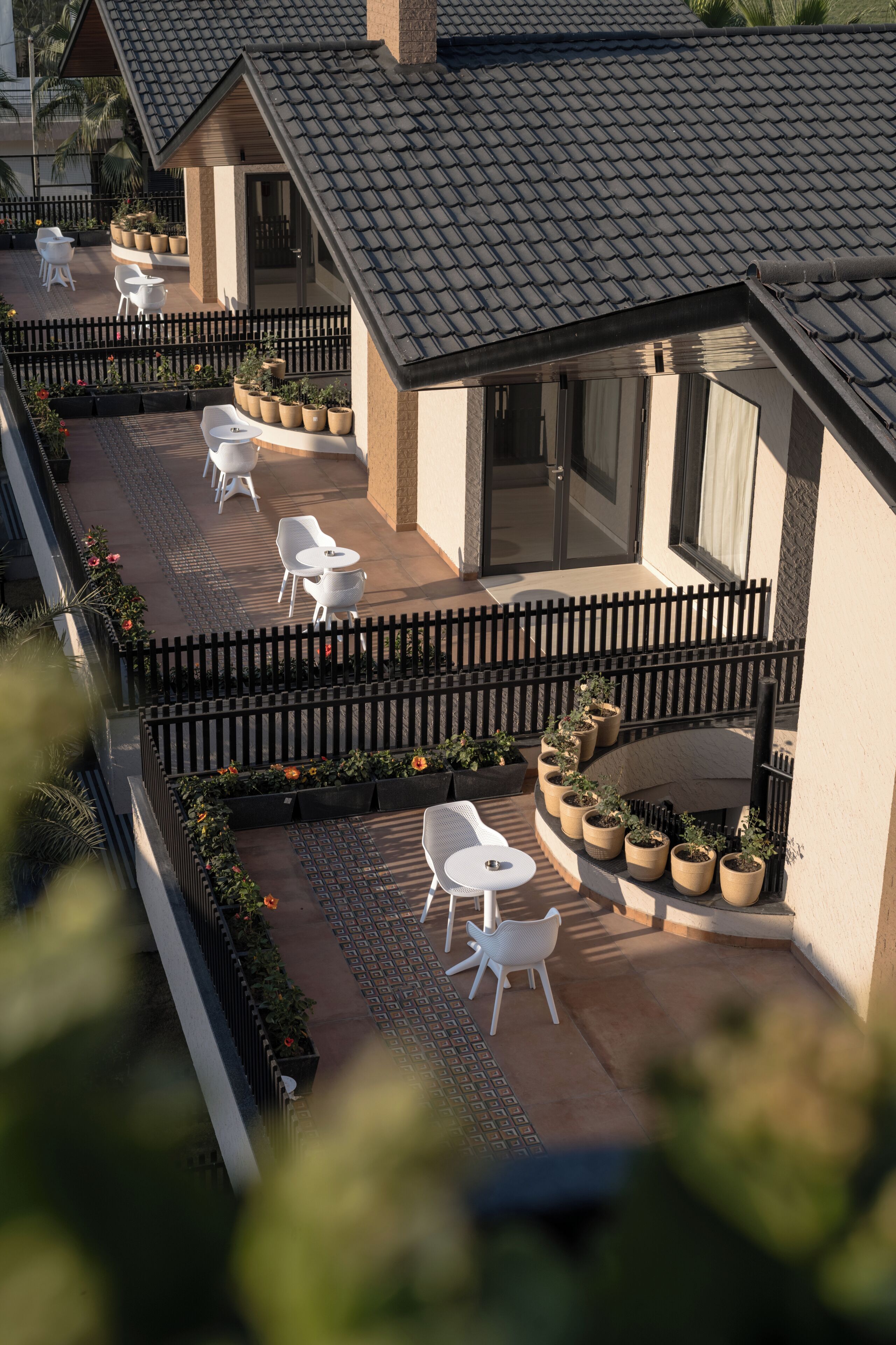 A rooftop patio with white chairs and potted plants, surrounded by a wooden fence.