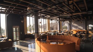 A spacious indoor area with a large orange sofa, multiple tables, and chairs arranged for dining or socializing. - Villasita (Haridwar)