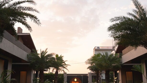 A hotel courtyard with palm trees, a central archway, and a pathway leading to the entrance. - Villasita (Haridwar)
