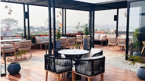 An outdoor patio area with wooden flooring, wicker furniture, and potted plants. - Villasita (Haridwar)
