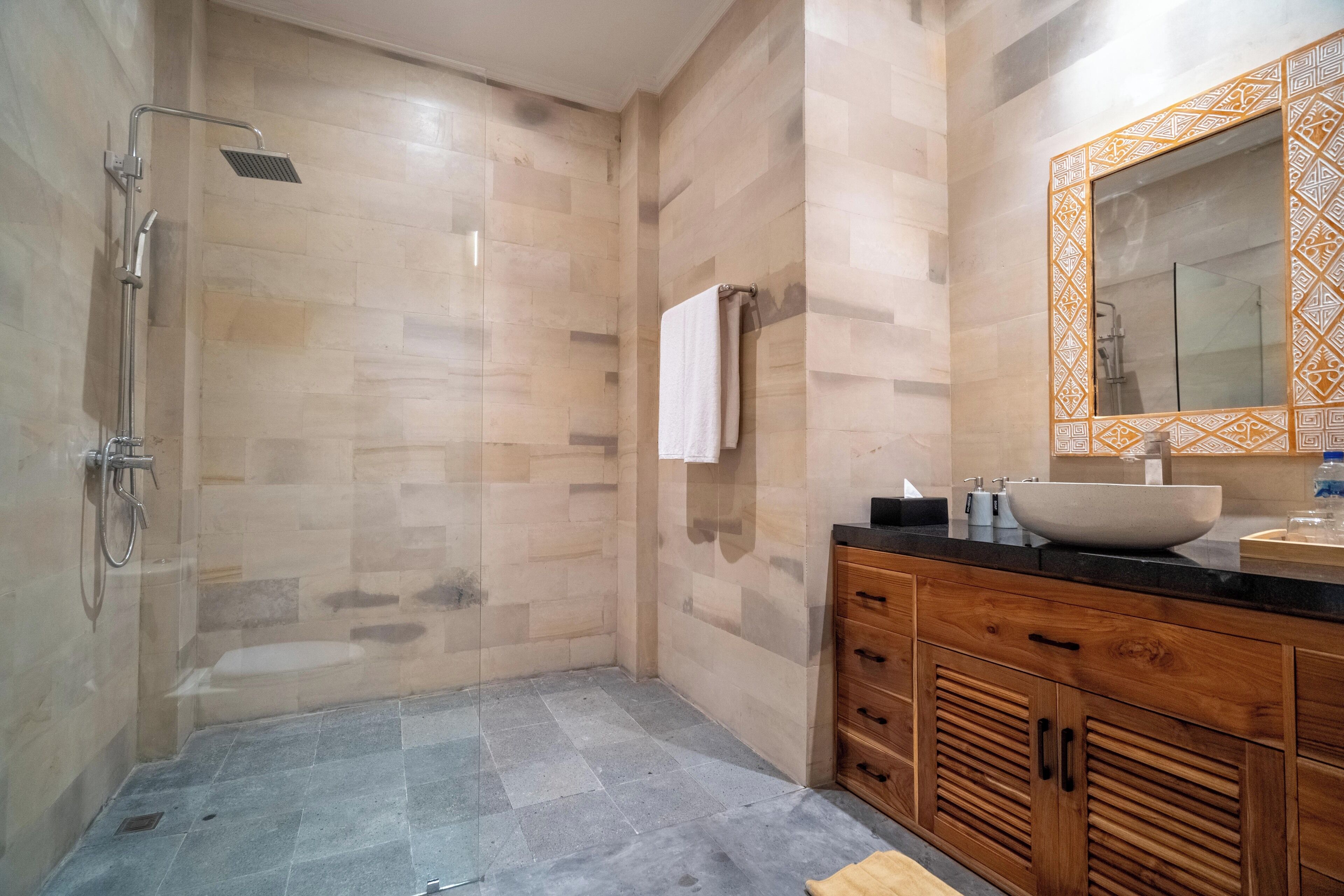 Un bagno moderno con doccia vetrata, un mobile lavabo in legno e un ampio specchio, e un pavimento piastrellato.