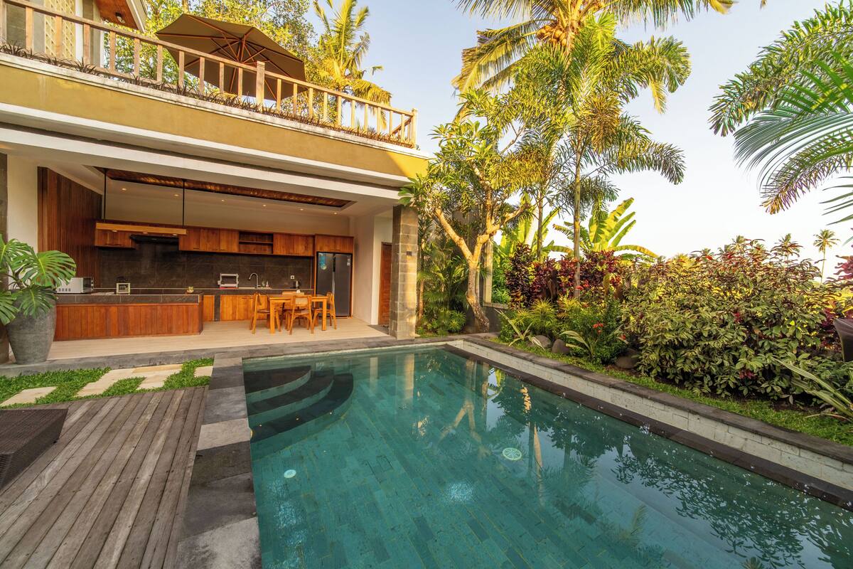 Una casa moderna con piscina, terraza de madera y plantas tropicales.