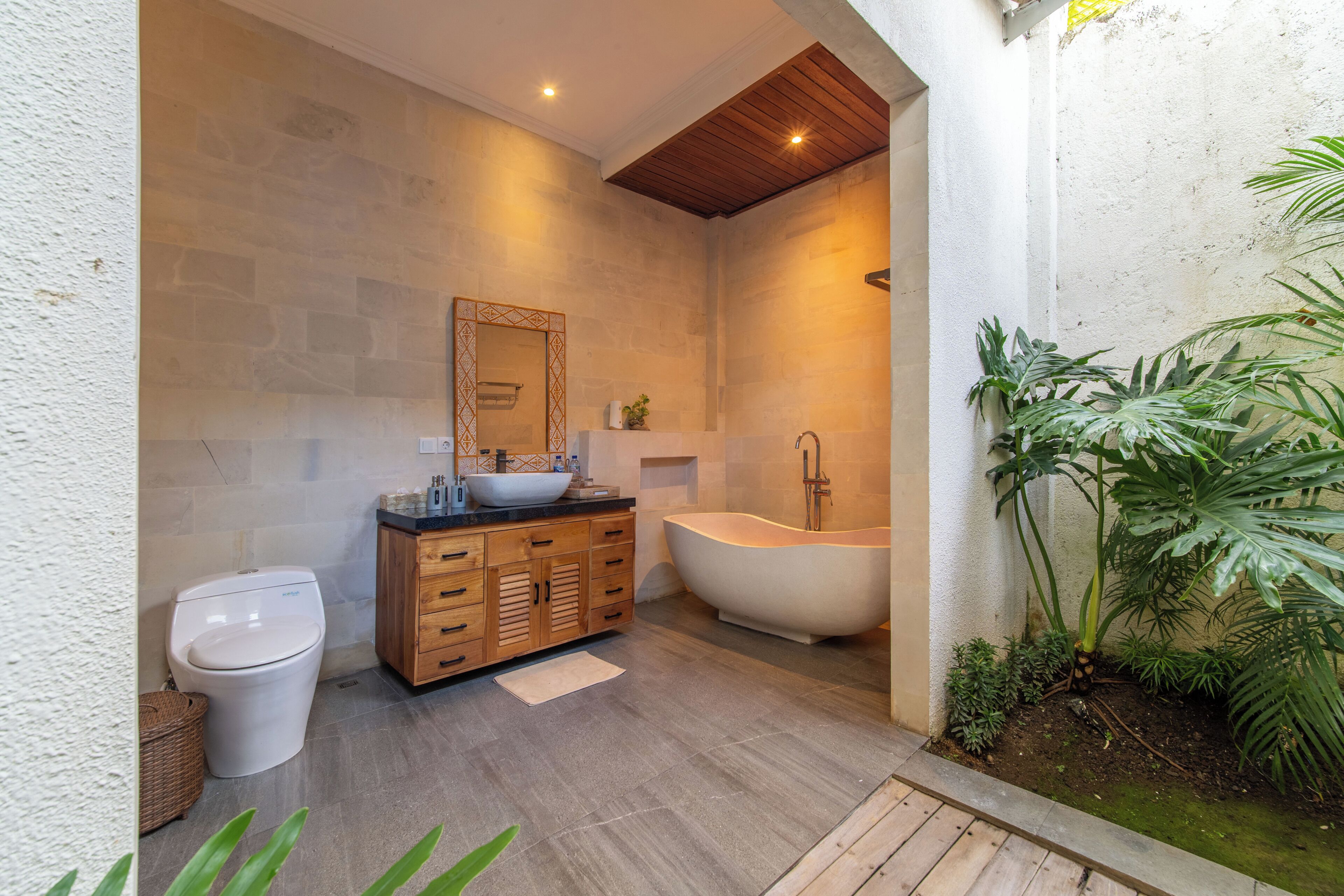 Un baño moderno con una bañera independiente, un mueble de tocador de madera y un espejo grande.