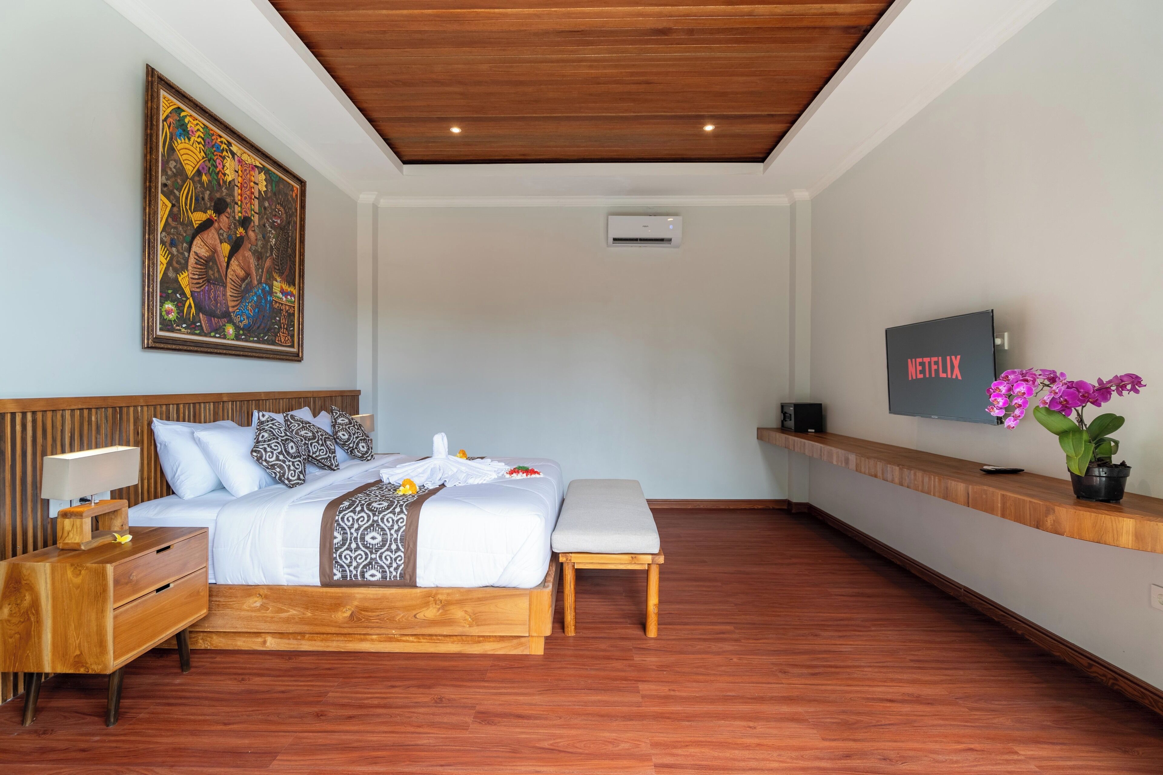 A modern bedroom with a wooden bed, a bedside table, a bench, a TV, and a wall-mounted air conditioner.