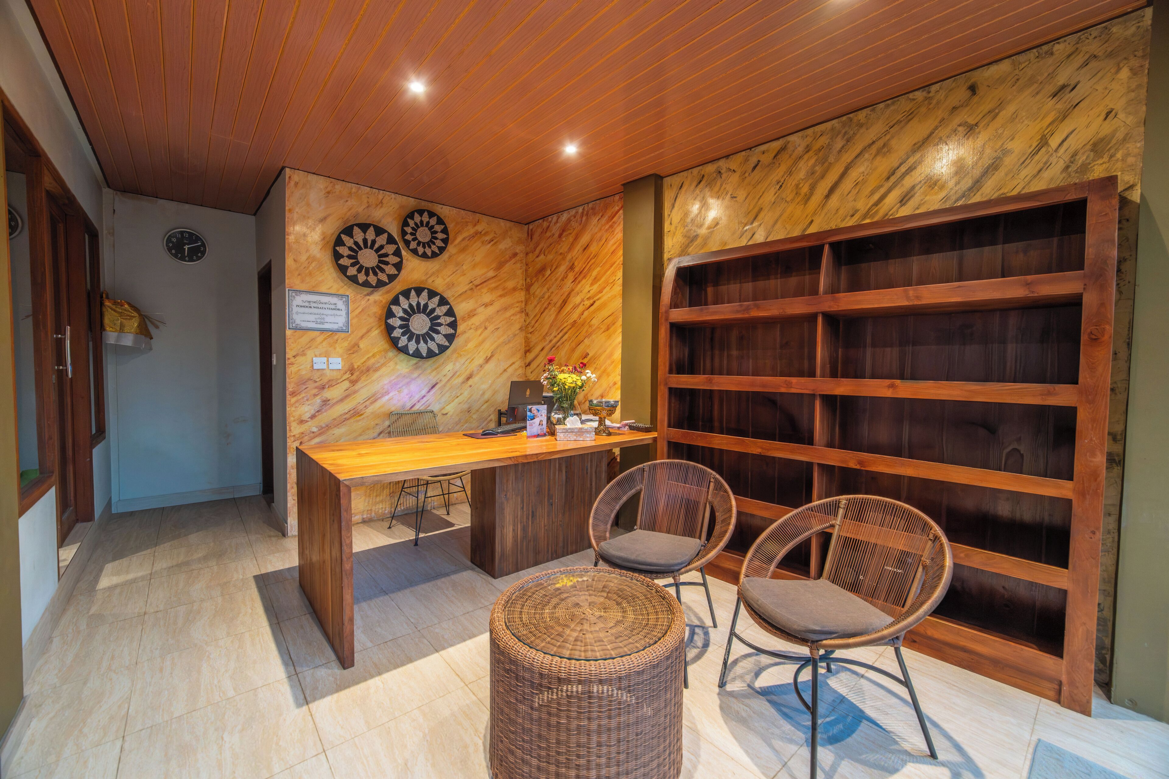 Una habitación con techo de madera, un escritorio con sillas, una pared decorada con placas y una estantería.