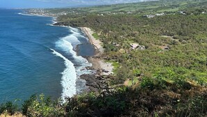 A coastal landscape with a beach, forested hills, and a clear sky.