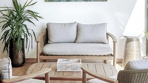A living room with a sofa, coffee table, and chairs. There is a large plant and a wall art piece.