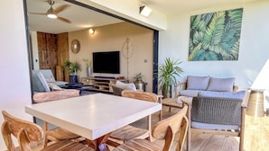 A modern living room with a flat-screen TV, wooden furniture, and a large plant.