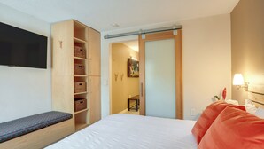 Habitación de hotel con una cama, un banco, un televisor, un armario y una puerta corredera que da al baño.