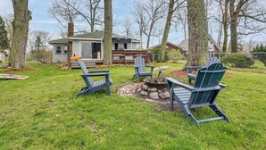 A backyard with a fire pit, Adirondack chairs, and a house in the background. - Secluded Home w/ Lake View in Delton! (Delton)