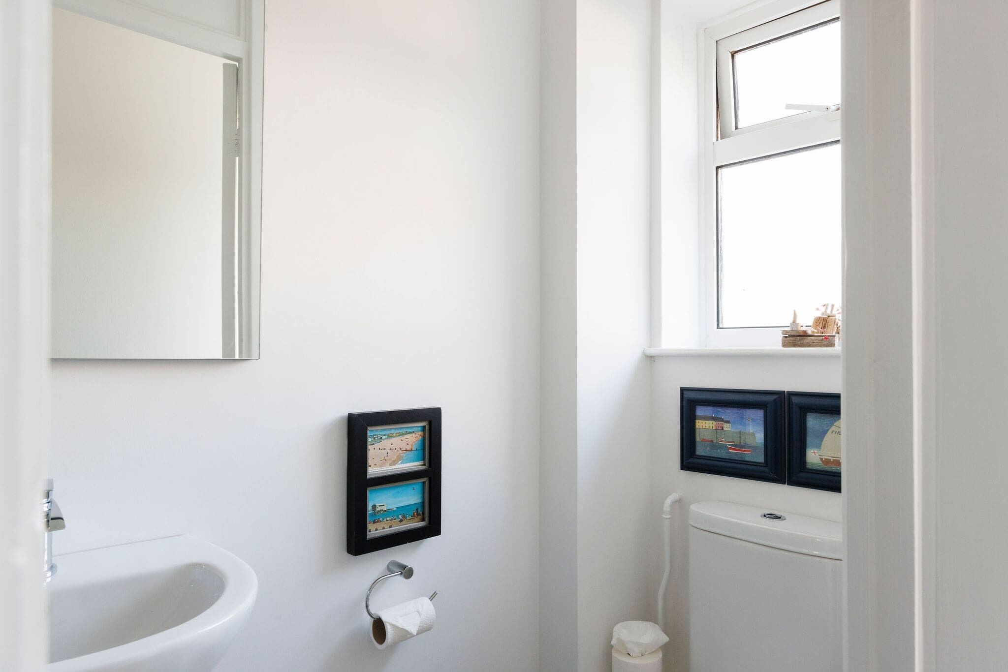 A bathroom with a white sink, a toilet, and framed pictures on the wall.