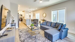 A modern living room with a grey sectional sofa, a coffee table, and a patterned rug. There is a TV on a stand, a small side table with a vase, and a ceiling fan. - 2 Mi to Duke University: Townhome in Durham! (Durham)