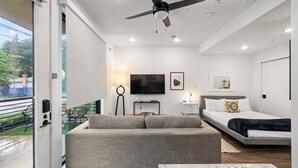 Ein modernes Hotelzimmer mit Sofa, Bett, Fernseher und einem Balkon mit Außenmöbeln.