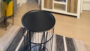 Una sala de estar con televisor sobre un mueble de madera, una mesita redonda y una planta en maceta.