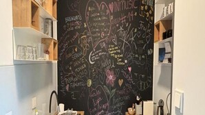 Una cocina con una pizarra llena de notas y dibujos escritos a mano, estantes de madera y un lavamanos de acero inoxidable.