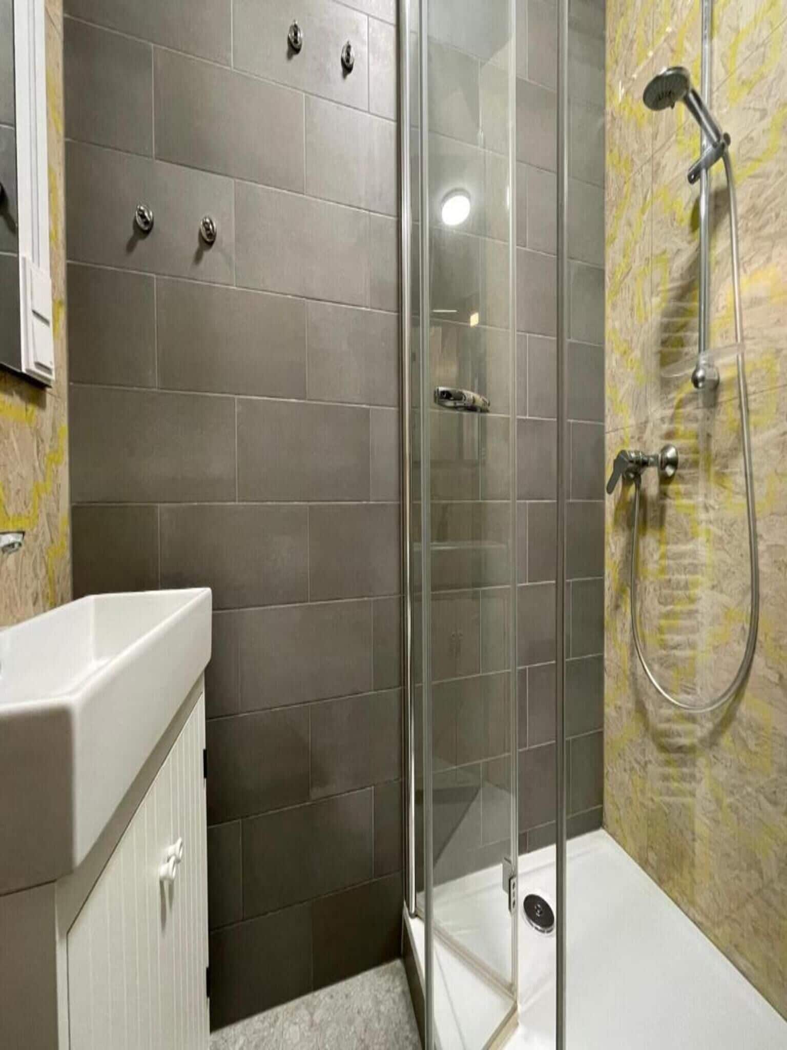 A modern bathroom with a glass-enclosed shower, a white sink, and a tiled wall.