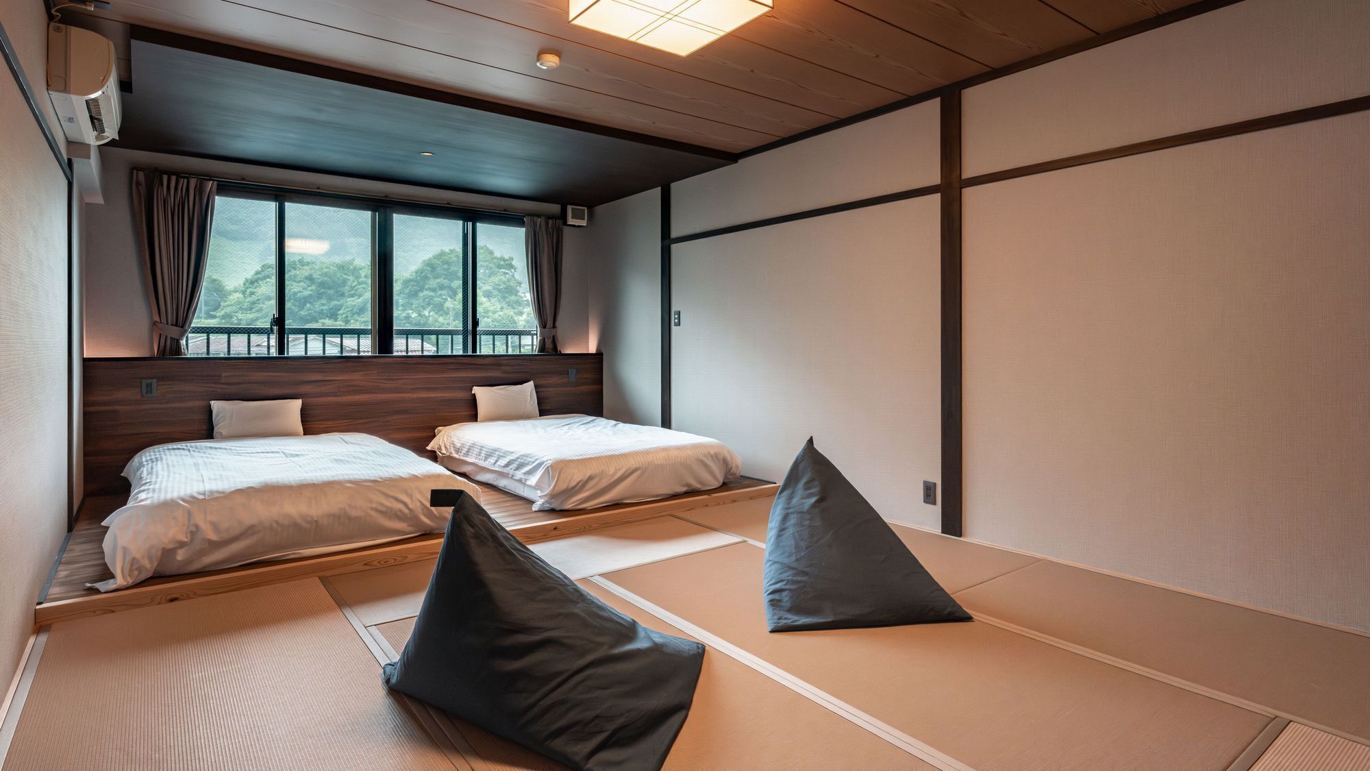 A traditional Japanese-style room with tatami mats, two beds, and a view of greenery outside.