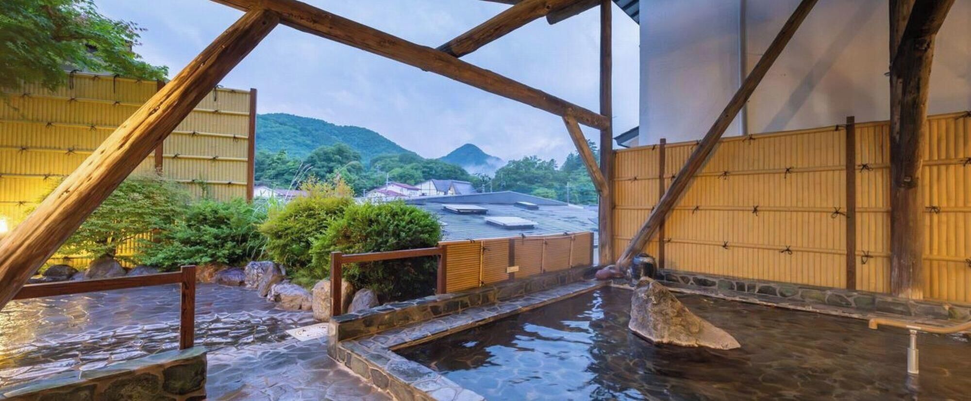 A traditional Japanese onsen with wooden beams, stone steps, and a view of surrounding buildings and hills.