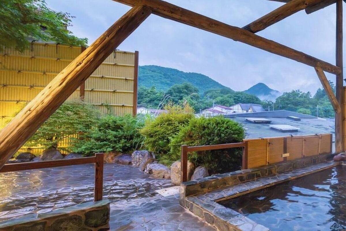 A traditional Japanese onsen with wooden beams, stone steps, and a view of surrounding buildings and hills.
