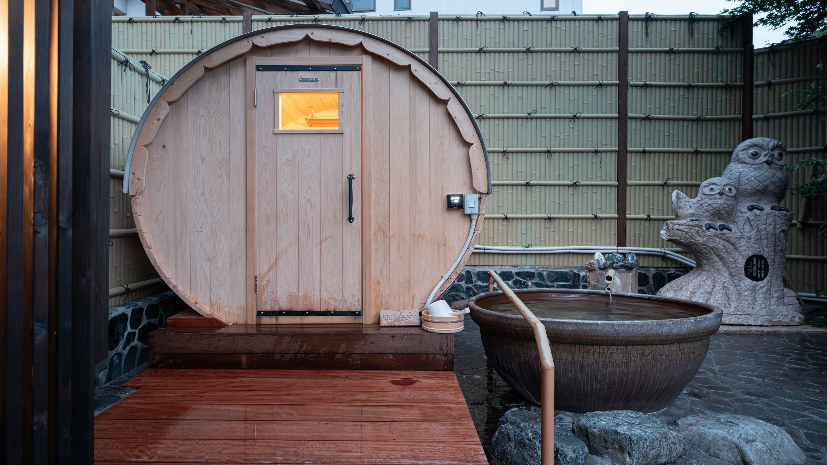 A traditional wooden sauna with a large door, a stone basin, and a stone sculpture.