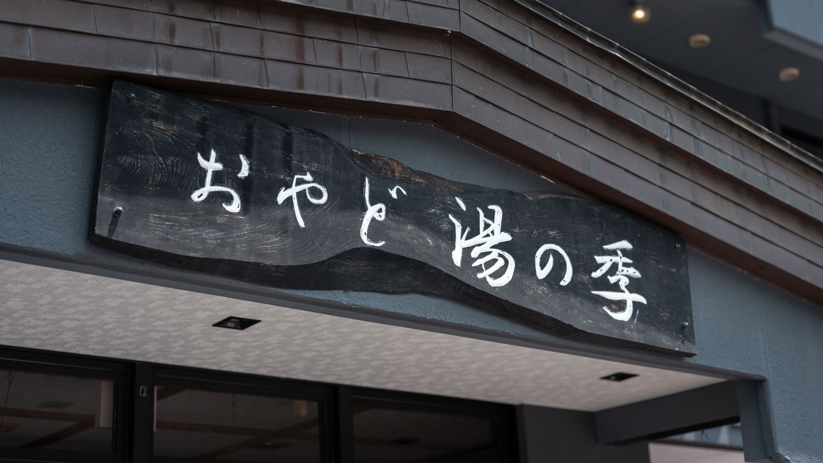 A building with a sign that reads "おやすみの亭" in white characters on a black background.